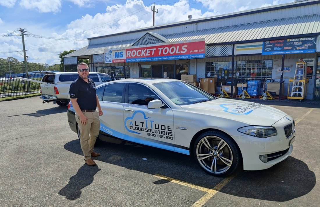 ACS director beside an Altitude Cloud Solutions branded car at a local business